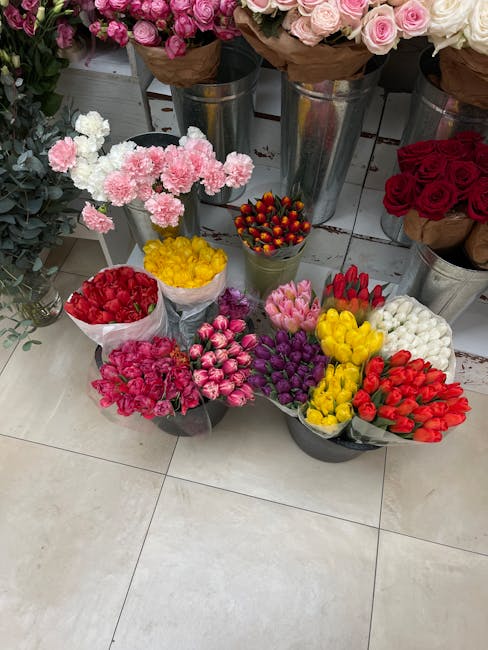An assortment of fresh flower bouquets arranged on a display floor in a flower shop, including pink carnations with ruffled petals, clusters of red, yellow, purple, white, and pink tulips, and small b