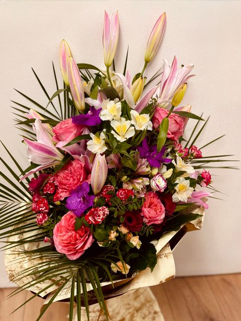 A vibrant floral bouquet featuring pink lilies with partially opened petals, large pink roses with tightly layered petals, white daffodils with yellow centers, small purple orchids, and red and white 